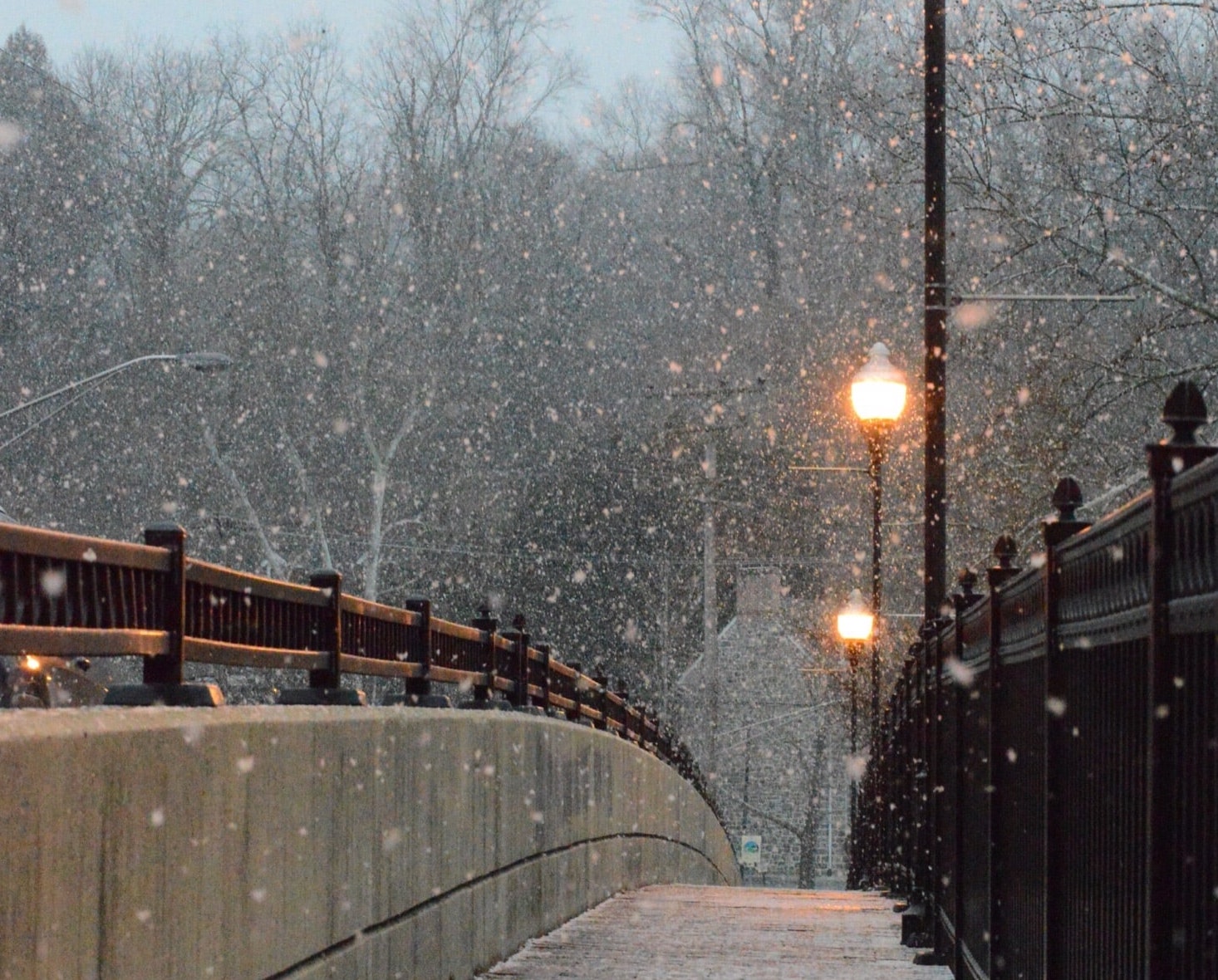 falling snow at dusk on a bridge Photo by Aaron Wilson of Unsplash.